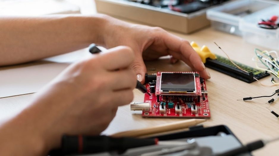 Técnico fazendo microssoldagem em uma placa de celular, sob lupa na bancada.
