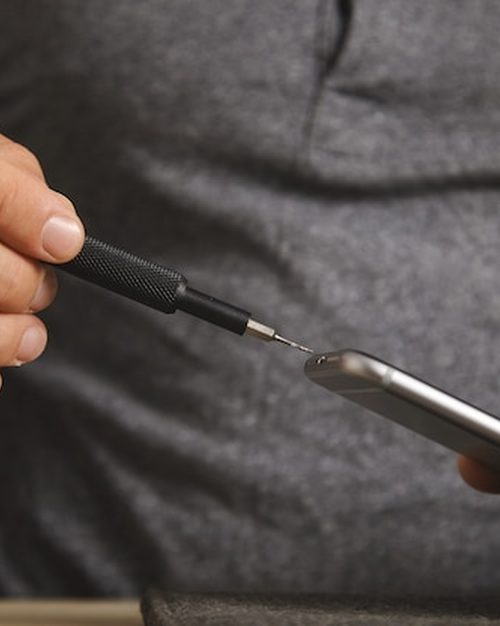 iPhone com a tela nova ligada, mostrando uma imagem nítida, ao lado das ferramentas de troca na bancada da loja.