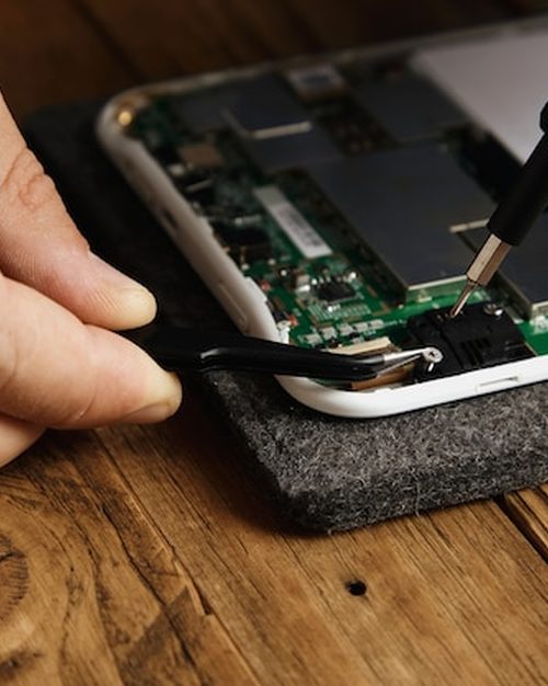 Técnico instalando uma bateria nova em um iPhone aberto na bancada de reparos.
